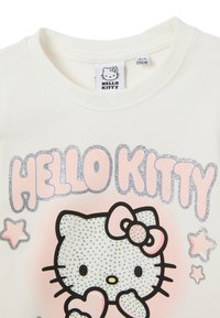 Witte katoenen t-shirt met een "Hello Kitty"-afbeelding in roze, versierd met zilveren glitters en kristalachtige details, ronde halslijn.