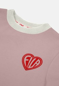 Sudadera de manga corta, de color rosa claro, con cuello de canalé blanco. Presenta un logo de corazón rojo con "FILA" en fuente blanca bordado en la parte frontal.