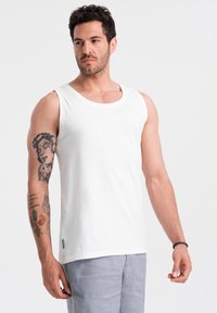 Débardeur en coton blanc avec un col rond, coupe décontractée et une petite étiquette sur le côté inférieur. Texture lisse, design minimal.