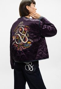 Σακάκι μπομπέρ σε μπορντό ραμμένο με παχιές ραφές, που διαθέτει ζωντανά κεντημένα σχέδια, στρογγυλό γιακά και αντίθετη γκρι περιφρόνηση. Σκούρα τζιν με ραφές ενίσχυσης.