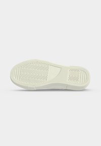 Semelle de chaussure blanche avec motifs en zigzag et lignes texturées pour l’adhérence, vue par dessous sur un fond uni.