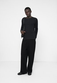 Melna ribota garām piedurknēm krekls ar pogu rindu, apvienots ar plašām melnām biksēm un melniem slip-on apaviem. Minimalistisks, monohroms apģērbs.