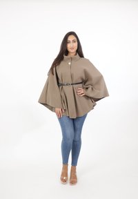 Brun, strukturerad kappa med hög krage och en knapp, bältad vid midjan. Matchas med blå denim och transparenta klacksandaler.