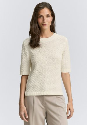 Pull en crème à manches courtes avec un motif de tricot texturé, col et poignets côtelés, associé à un pantalon taille haute beige.
