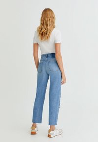Jean en denim bleu taille haute avec une coupe droite, ourlets effilochés et poches appliquées, associé à des baskets blanches.