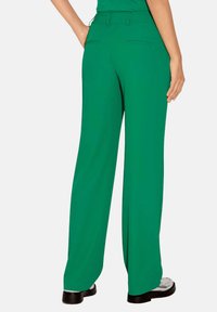 Groene wijde broek van soepel materiaal, met een hoge taille, achterzakken en een losse pasvorm, gecombineerd met zwarte plateau schoenen.