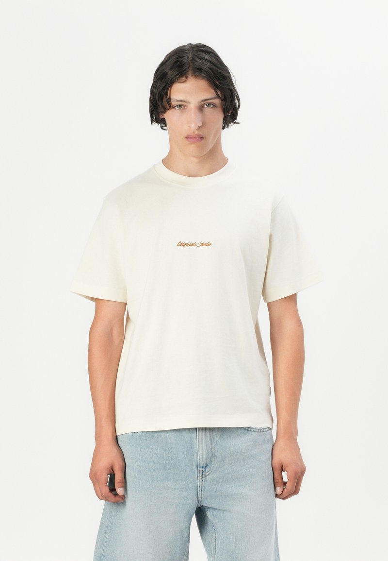 Tricou din bumbac de culoare crem, cu mâneci scurte, având un logo brodat subtil în nuanțe de portocalie. Construit cu un croi lejer și decolteu rotund.
