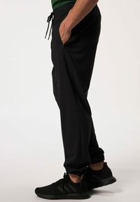 Joggers deportivos negros con cintura ajustable, bolsillos laterales con cremallera y piernas ajustadas, combinados con zapatillas negras. Textura de tela suave.