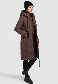 Geaca puf din brun, cu glugă, având matlasare în formă de V, accente negre, buzunare laterale și închidere cu fermoar. Asortată cu colanți negri și cizme.