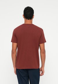 Μαρόν κοντομάνικο μπλουζάκι με στρογγυλή λαιμόκοψη, φτιαγμένο από μαλακό ύφασμα. Λείος υφασμάτινος χαρακτήρας, απλός σχεδιασμός, χωρίς ορατά σχέδια ή προσθήκες.