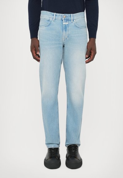 Helle blaue Jeans mit geradem Schnitt, featuring einen Knopfverschluss, fünf Taschen und dezenten Ausbleichungen an den Oberschenkeln. Schwarze Sneakers runden den Look ab.