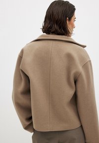 Beige wool-blend jacket with a wide collar, dropped shoulders, and a cropped hem. Soft texture and minimalistic design.