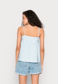 Top azul claro, sem mangas, com um padrão texturizado, design franzido e alças ajustáveis; combinado com calções de ganga com bainha dobrada.