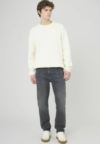 Pull en tricot blanc avec un col rond, associé à un jean gris foncé et des baskets blanches. Design simple, texture douce et coupe décontractée.
