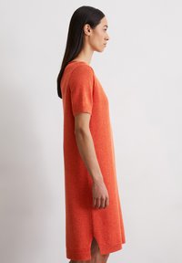 Robe en tricot orange à manches courtes, coupe décontractée, fentes sur les côtés et ourlet côtelé. Texture lisse, longueur au genou.
