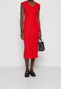 Punainen bodycon-mekko lyhyillä hihoilla, polvipituinen, valmistettu sileästä kankaasta. Yhdistetty mustiin loafereihin ja pieneen mustaan käsilaukkuun.