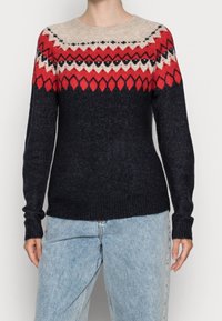 Neulepusero, jossa yläosassa kerma-, punainen ja musta geometrinen kuvio. Tummansininen runko, jossa resorit hihansuissa ja helmassa, valmistettu villasekoitteesta.