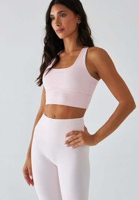 Jasnoróżowy sportowy stanik i legginsy z wysokim stanem, wykonane z rozciągliwej tkaniny, charakteryzujące się gładką fakturą i minimalistycznym wzornictwem bez wzorów.