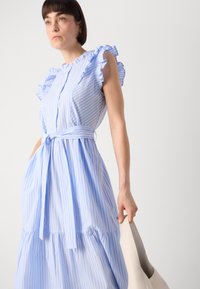 Hellblau gestreiftes Kleid mit Rüscheärmeln und einem Bindegürtel, ausgestattet mit einem mehrlagigen Rock und Taschen. Glattes Material mit einer soften Textur.