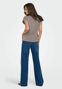 Top corto gris de manga corta combinado con pantalones de mezclilla azul de pierna ancha. La tela parece suave, con un ajuste relajado y un caído sutil.