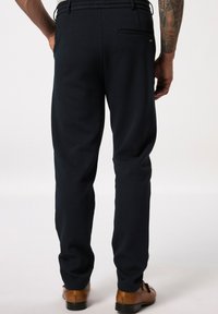 Marineblauen Hosen aus strukturiertem Stoff, mit geradem Bein und Gesäßtasche. Getragen mit braunen Schuhen, die ein klassisches Design aufweisen.