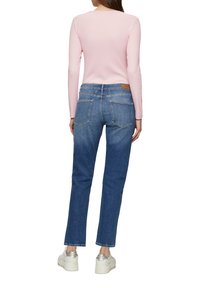 Hellrosa langärmliges Oberteil, kombiniert mit blauen Jeans aus Denim mit Gesäßtaschen, geradem Bein und fransigem Saum, getragen mit silbernen Sneakers.