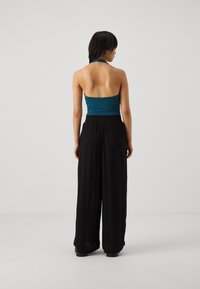 Tyrkysový halter top s otvoreným chrbtom v kombinácii s čiernymi širokými nohavicami; hladká látka a elastický pás pre pohodlie a voľnosť pohybu.