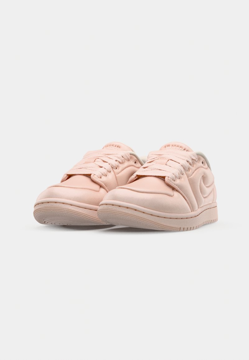 Zapatillas de deporte rosa claro con un acabado mate suave, punta redondeada y suela de goma texturada. Presentan un diseño de cordones y acentos con logotipo.