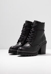 Svarta läderankleboots med hög klack, snörningsdesign, dekorativ söm längs sulan och texturerad gummisula.