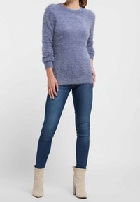 Ljuslila tröja med en fluffig textur, rund halsringning och långa ärmar, i kombination med åtsittande blå jeans och beige ankelstövlar.