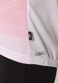 Krótki rękaw sportowa koszulka w białym kolorze z różowymi poziomymi paskami, wykonana z teksturowanej tkaniny, z zaokrąglonym dolnym brzegiem oraz logami "AEP" i "QWIC" na boku.