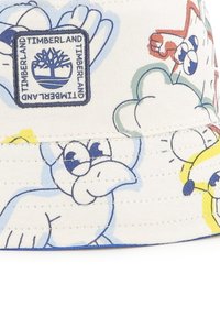 Cappello a secchiello in morbido cotone bianco con stampe di animali cartoni animati colorati. Presenta un bordino blu e una toppa con il logo Timberland sulla parte anteriore.