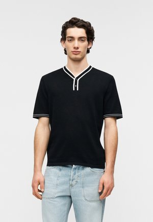 Tricou polo negru cu mânecă scurtă, cu decolteu în V, având margini albe pe guler și mâneci, și o fenta cu două nasturi.