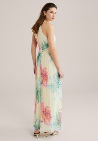 Maksimekko, jossa on kevyt ja ilmava kangas, pastellinkeltainen tausta ja suuret kukkakuviot vaaleanpunaisena ja turkoosina. Hieno laskostus koristaa hameen.