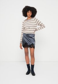 Dryžuotas smėlio ir pilkos spalvos megztinis su ilgomis rankovėmis, derinamas su tamsiai mėlyna satino suknele, kurios apačioje yra juodos nėrinių detalės. Modelis dėvi juodus batus ir kojines.