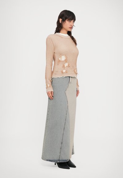 Béžový rebrovaný pletený sveter s opranými detailmi, skombinovaný s dlhou patchworkovou rifľovou sukňou v svetlo sivej, tmavo sivej a béžovej farbe.