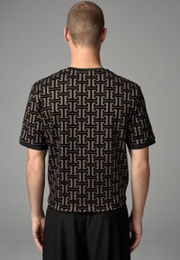 Camisa de punto de manga corta en tonos negros y marrones con un diseño geométrico, con cuello redondo y puños negros en contraste.
