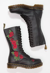 Botas de combate de cuero negro con bordado de rosa roja, diseño de cordones, cremallera lateral, suela de goma y acentos de costura amarilla.