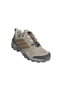 Scarpa da trekking leggera beige con accenti in gomma grigia, tomaia in mesh e design con strisce marroni. Presenta un sistema di allacciatura rapida e suola aggressiva.