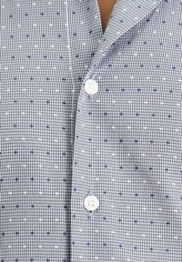 Camicia a maniche corte in un motivo a quadretti blu navy e bianchi con piccoli puntini blu e bianchi. Presenta un colletto a punte e bottoni bianchi.