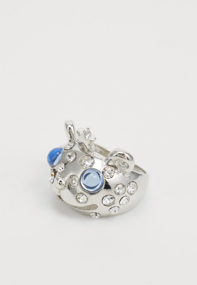Bague en argent avec un motif de poisson, ornée de deux pierres bleues et de nombreux strass pour la texture et l'éclat. Forme lisse et arrondie.