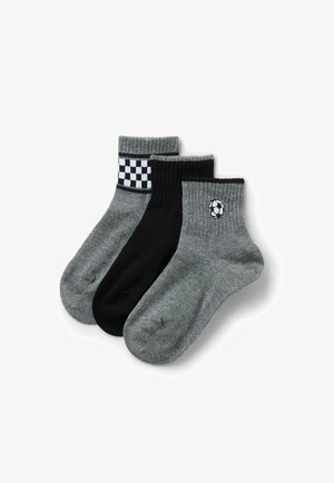 Trzy skarpetki do kostki w kolorach czarnym i szarym; jedna szara z czarno-białą kratkowaną lamówką, jedna całkowicie czarna oraz jedna szara z emblematem piłki nożnej w czarno-białym kolorze.