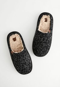Black and gray knitted slippers with a soft beige lining, rounded toes, and a flat sole. Features a small brown logo accent.