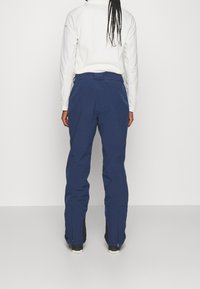 Mörkblå skidbyxor med rak modell, dragkedja vid benslut och ett texturerat tyg. Inkluderar bakfickor och detaljer med bälteshällor.