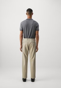 Men's gray patterned short-sleeve polo shirt with black trim, paired with beige chinos. Black shoes complement the outfit.