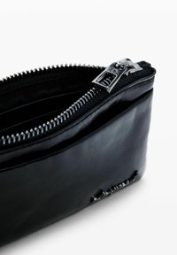 Bolsa de cuero negro con textura suave, con una cremallera plateada y una forma ligeramente curva. Compartimentos visibles en el interior.