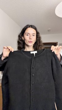 Cardigan noir en matière douce, avec un col rond, une fermeture par boutons sur le devant et des manches longues. Texture lisse sans motifs.