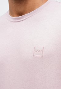 Ανοιχτό ροζ βαμβακερό T-shirt με στρογγυλή λαιμόκοψη και μικρό ορθογώνιο κεντημέν�ο λογότυπο στο κέντρο του στήθους. Ομαλή υφή.