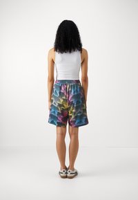 Barevné síťované šortky s vlnitým vzorem v modré, růžové a žluté barvě. Elastický pas. Nosené s obepnutým bílým tílkem a teniskami.