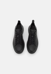 Black leather sneakers with a round toe, flat laces, and textured accents. Features a small heel and pull tab for easy wear.